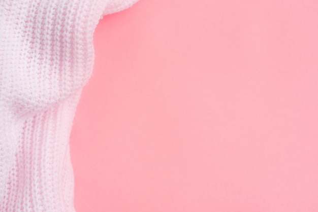 Pink knitted clothes on a pink paper background