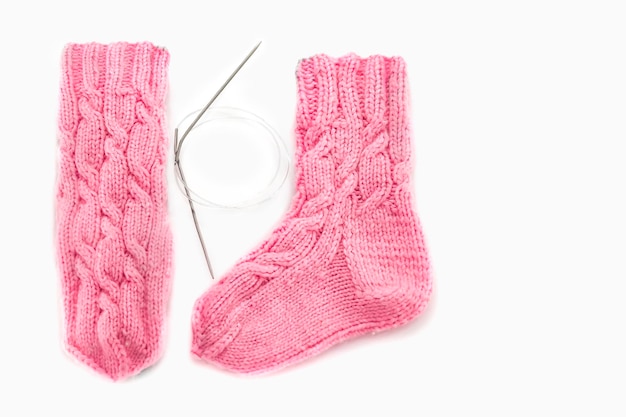 Pink knitted socks with Aran pattern and knitting needles on a white background Place for text