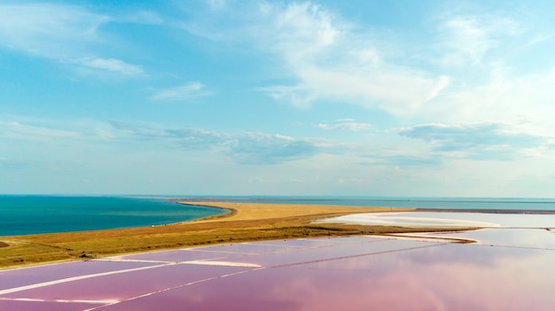 Pink lake and sandy beach with a sea bay under a blue sky with clouds