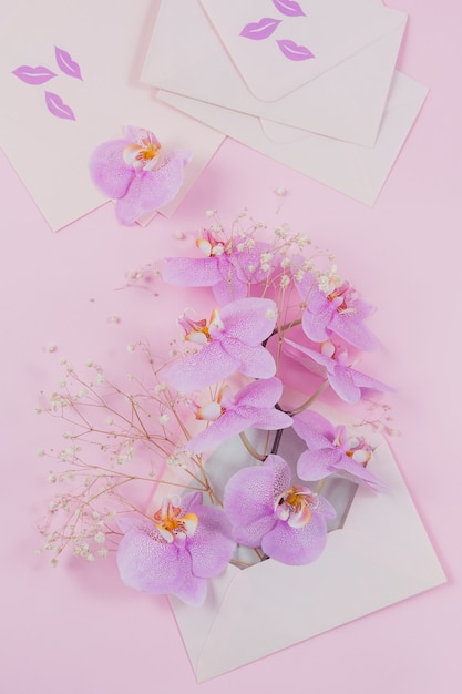 Pink letter full of flying orchid flowers and new empty envelops on light pink background