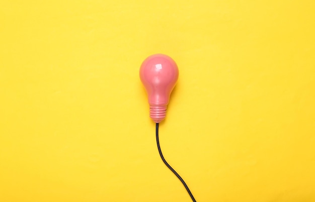 Pink light bulb with cable on yellow background Creative minimalism layout Fresh idea Concept art Flat lay Top view