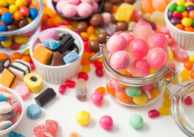 Pink lollipop candies in jar with various milk chocolate and jelly gums candies on white background