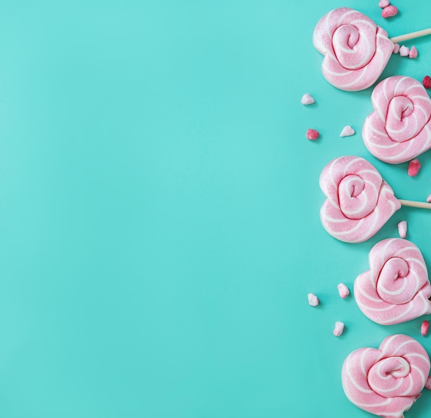 Pink lollipops in the shape of hearts with color sugar on a green background Top view and copy space