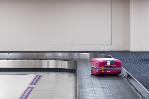 Photo pink luggage on the belt conveyor.