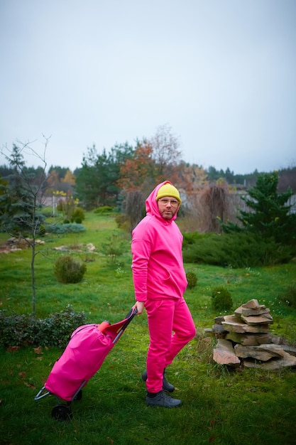 Pink man posing outdoor in pink sport suit with rolling bag Pink suit
