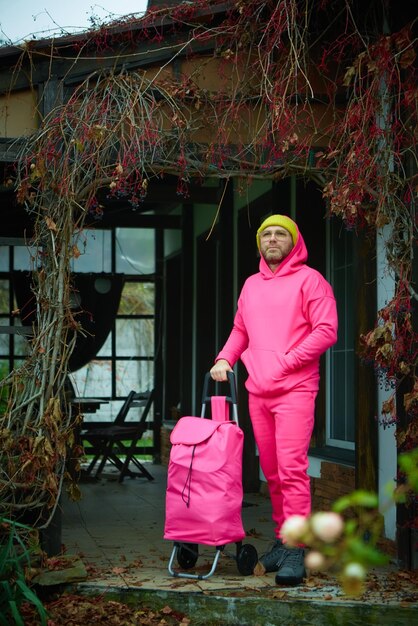 Pink man posing outdoor in pink sport suit with rolling bag Pink suit