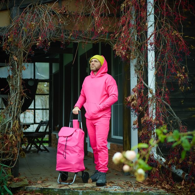 Pink man posing outdoor in pink sport suit with rolling bag