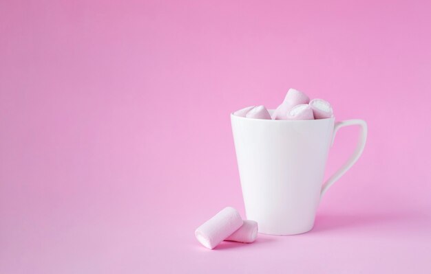 분홍색 배경에 흰색 컵에 핑크 멜로 과자.