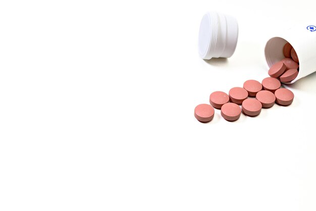 Photo pink medicine pills spilling out of a white bottle on white background.