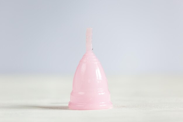Розовая менструальная чаша лежит на белом винтажном деревянном фоне.