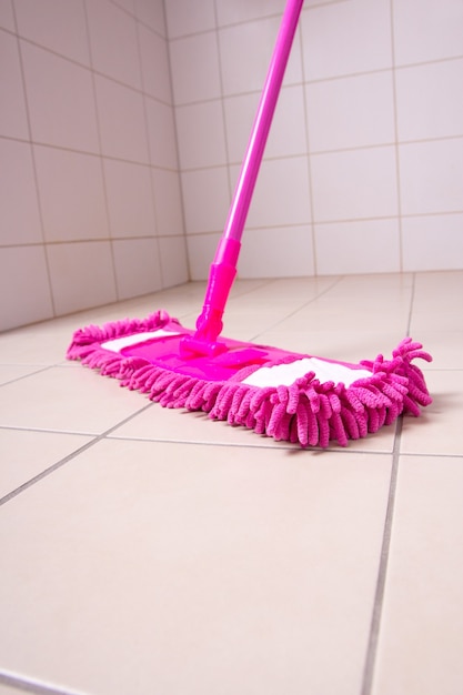 Pink mop cleaning light tile floor in bathroom