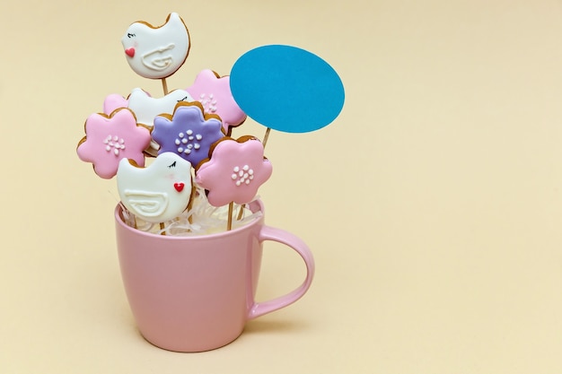 Pink mug with cookies on a skewers on a beige background. Food concept. Photo with place for your text and design.