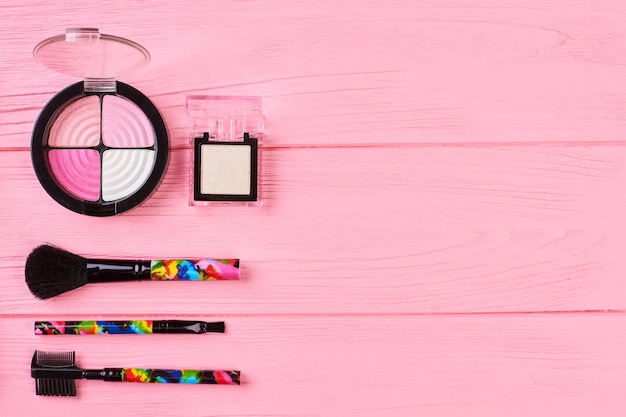 Foto ombretti rosa e neutri, copia spazio. set di ombretti colorati e pennelli glamour per il trucco. sfondo di legno rosa, spazio per il testo.