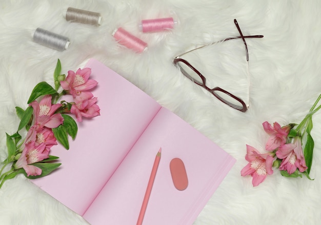 ピンクの花と赤いメガネの白い毛皮のような背景にピンクのノートブック紙