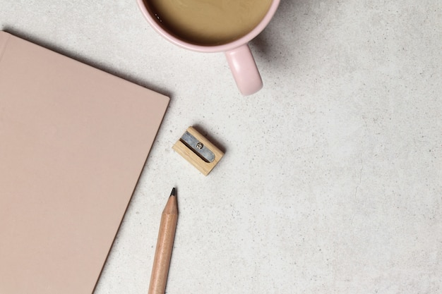 Pink notebook with wooden pencil, sharpener, cup of coffee on garnet texture