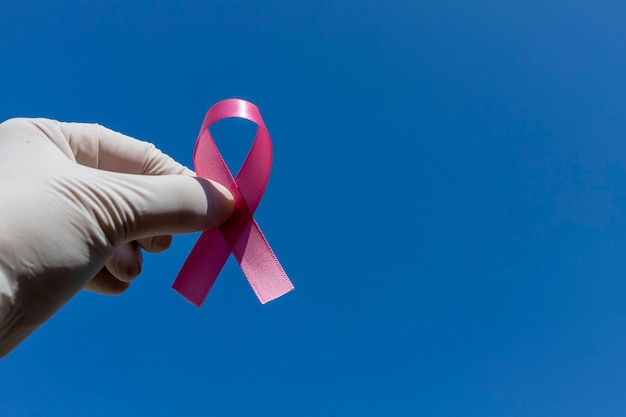 Pink October hand with surgical glove holding a pink bow breast cancer prevention campaign