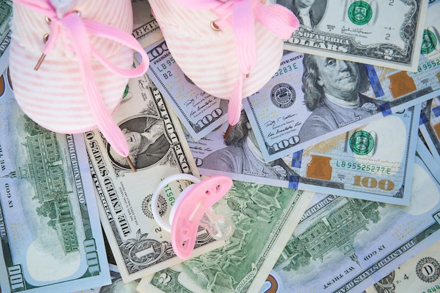 Pink pacifiers and children's shoes on the background of money