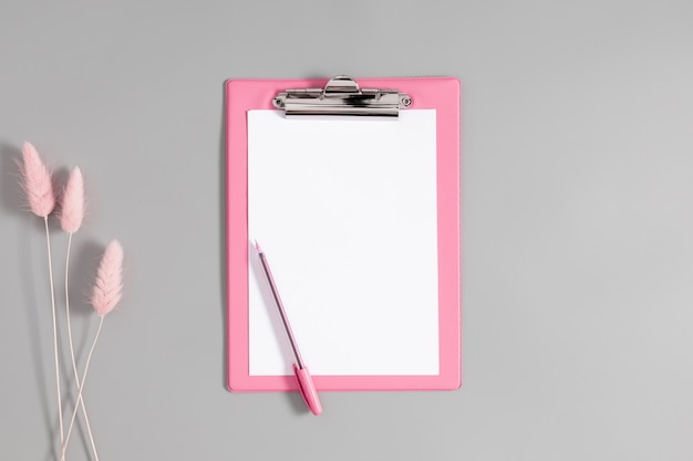 Pink paper clipboard and pink pen and pink plants isolated on gray background with copy space