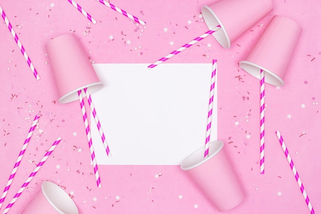 Pink paper cups striped drinking straws candy sprinkles with blank white card on pink background