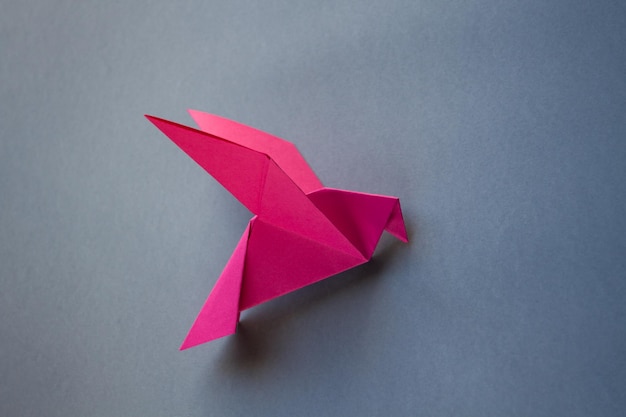 Origami di colomba di carta rosa isolato su sfondo grigio