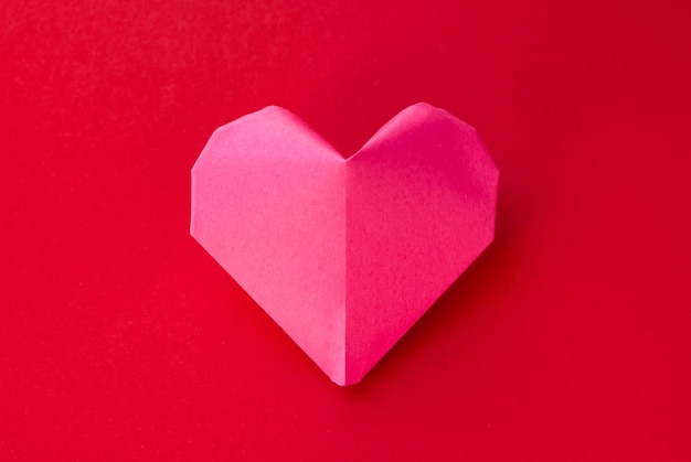 Pink paper heart origami isolated on a red background