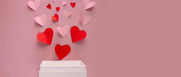 Foto carta rosa a forma di cuore su un piatto steso sul bordo della cornice che fuoriesce dalla confezione regalo bianca per banner di sfondo o cartolina per il giorno di san valentino