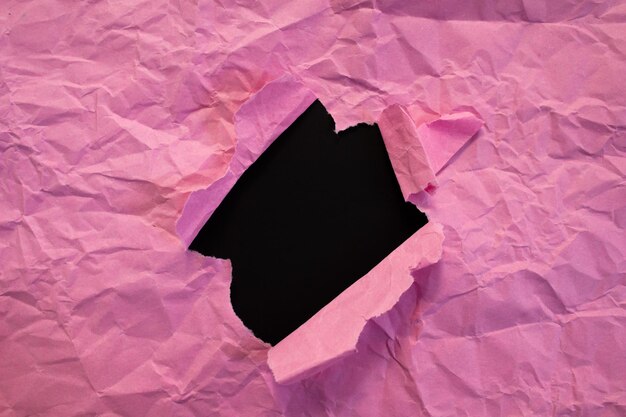 Pink paper hole on black background. Copy space for advertising text. Crumpled paper torn.