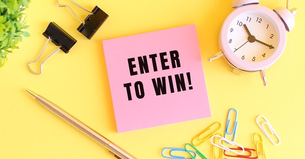 텍스트가있는 분홍색 종이 ENTER TO WIN. 시계, 노란색 표면에 펜