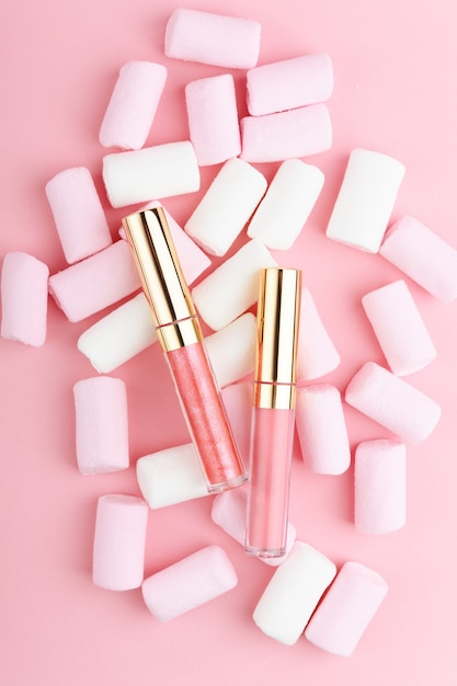 Pink pastel lip gloss on a background of sweets.