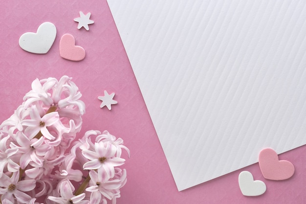 Pink pearl hyacinth flowers on colored paper wall with decorative hearts, copy-space