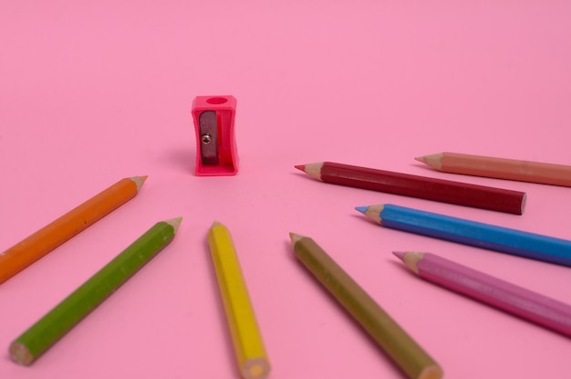 Pink pencil sharpener with several kinds of colored pencils on a pink background