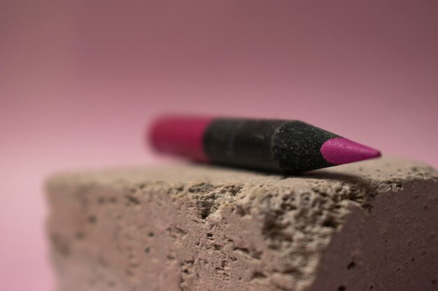 A pink pencil with a black tip sits on a concrete block.