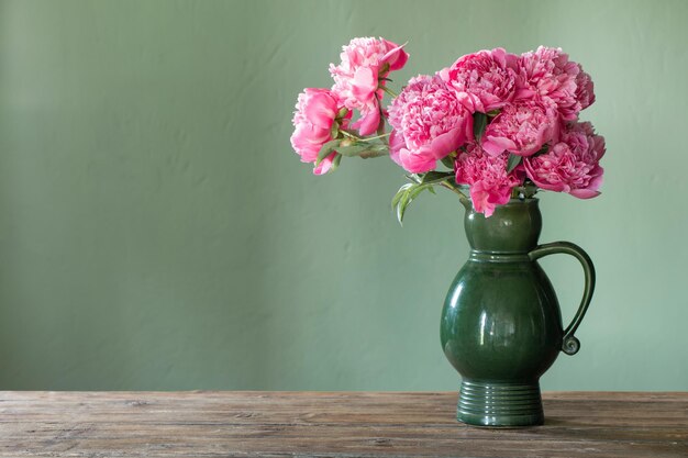 Photo pink peonies in ceramic jug on green background