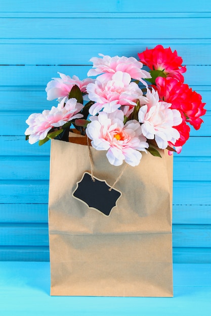 Pink peonies in a craft package with a chalkboard on a blue wooden table. Postcard for the holiday. 