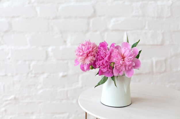 Pink peonies flowers bouquet on the table. White brick wall background flower shop interior
