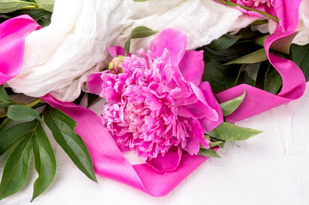 Pink peonies wrapped in a white fabric with a pink ribbon on a light stone