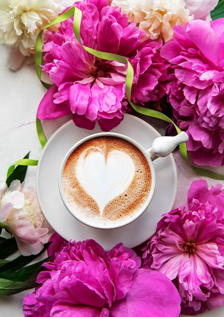 Pink  peony and cup of coffee  in beautiful style on white marble background. Floral background.  Top view