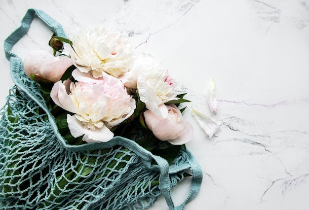 Pink peony in string bag  on white marble.