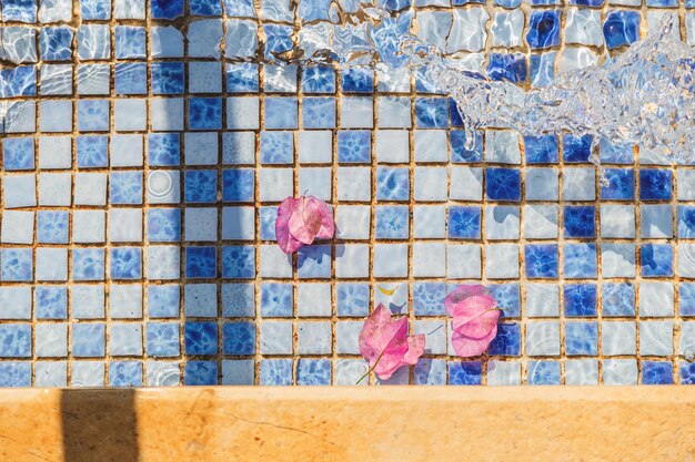 Photo pink petals in the pool water texture on blue tiles background