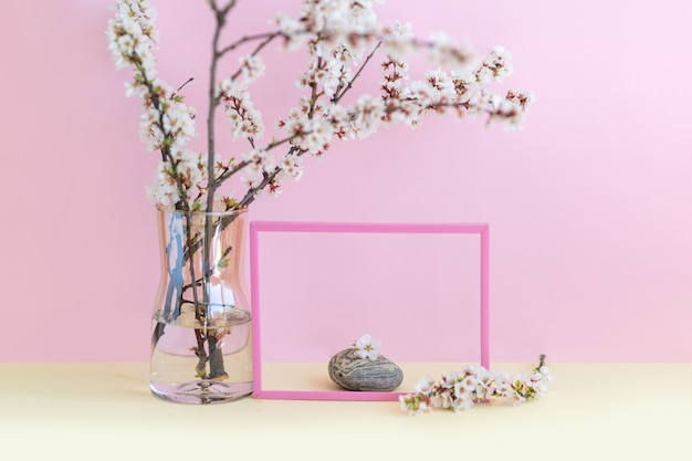 Pink photo frame and glass vase with a cherry flowers branches on a pink wall Minimalistic composition of natural materials