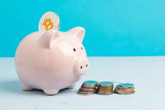 Pink piggy bank on blue space with bitcoin and coin