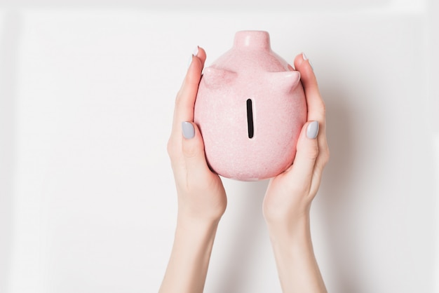 Pink piggy bank in female hands isolate on grey