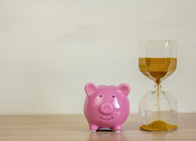 Pink piggy bank and hourglass on the table.Time is money.