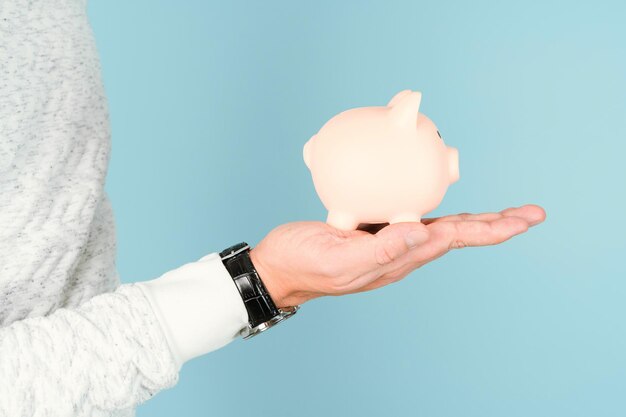 Pink piggy bank on a man's palm, blue background