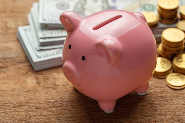 Pink piggy bank and money with banknotes and coins on a wooden table.