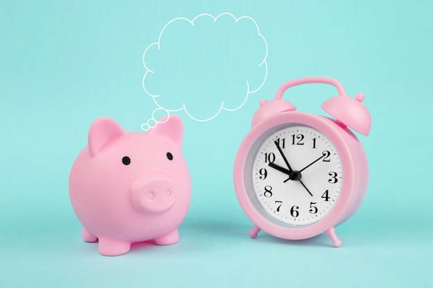 ピンクの貯金箱頭上に雲の思考と青い背景の時計と貯金箱。将来の投資と退職の概念のためのお金の節約。