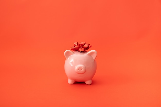 赤の背景にピンクの貯金箱。投資と節約のレシピ