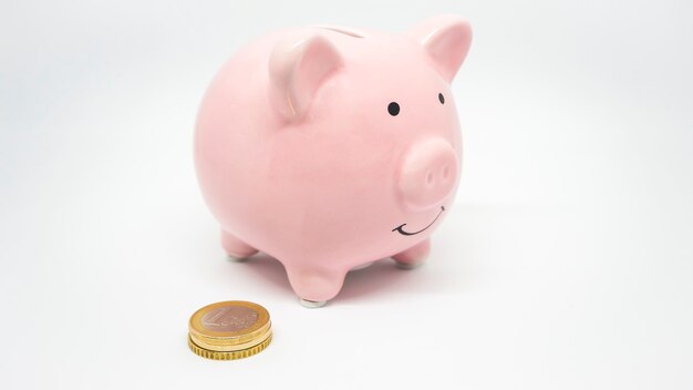ピンクの貯金箱は白い背景にコインを節約しますコインの時間のお金とビジネスコンセプトを節約します