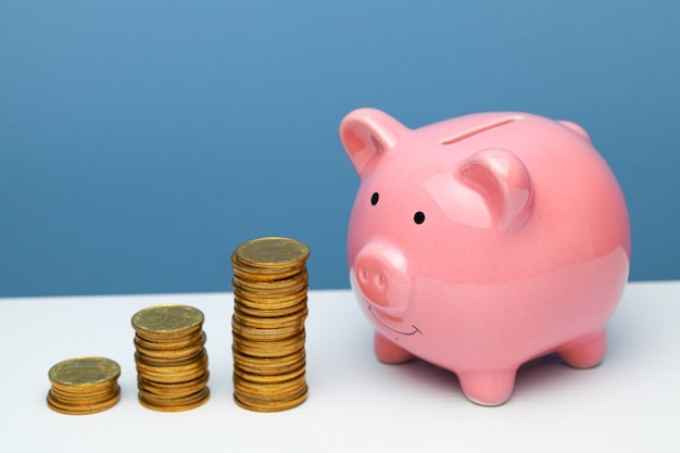 Pink piggy bank and a stack of coins on the steps on a table