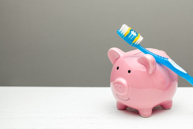 Pink piggy bank and toothbrush on gray background The concept of how to save on dental treatment